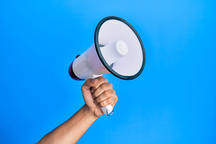 holding up a large megaphone against a color background
